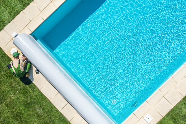 Ein Arbeiter arbeitet an einem Swimmingpool, während er die Rollabdeckung des Pools aufrollt.